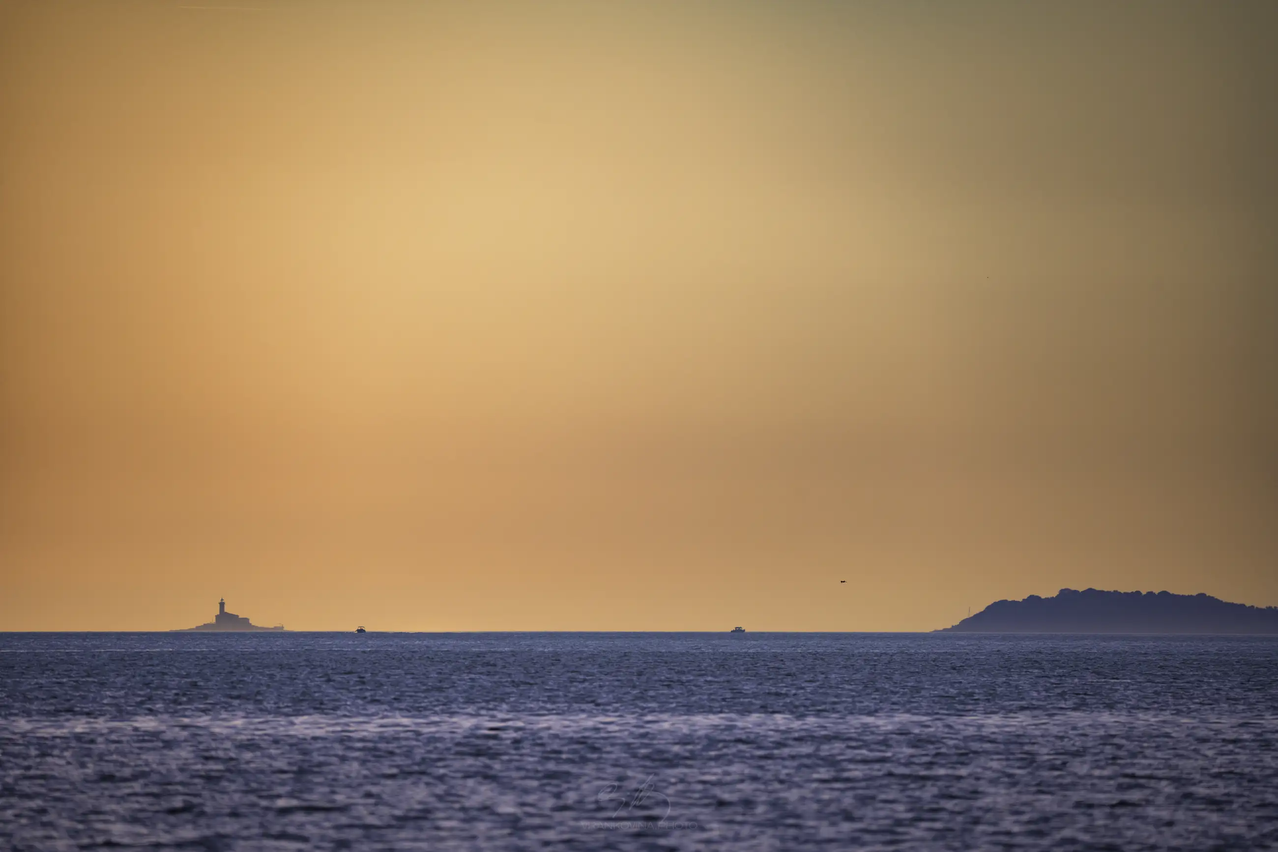 Sea horizon with a lighthouse, boats and an island at sunset