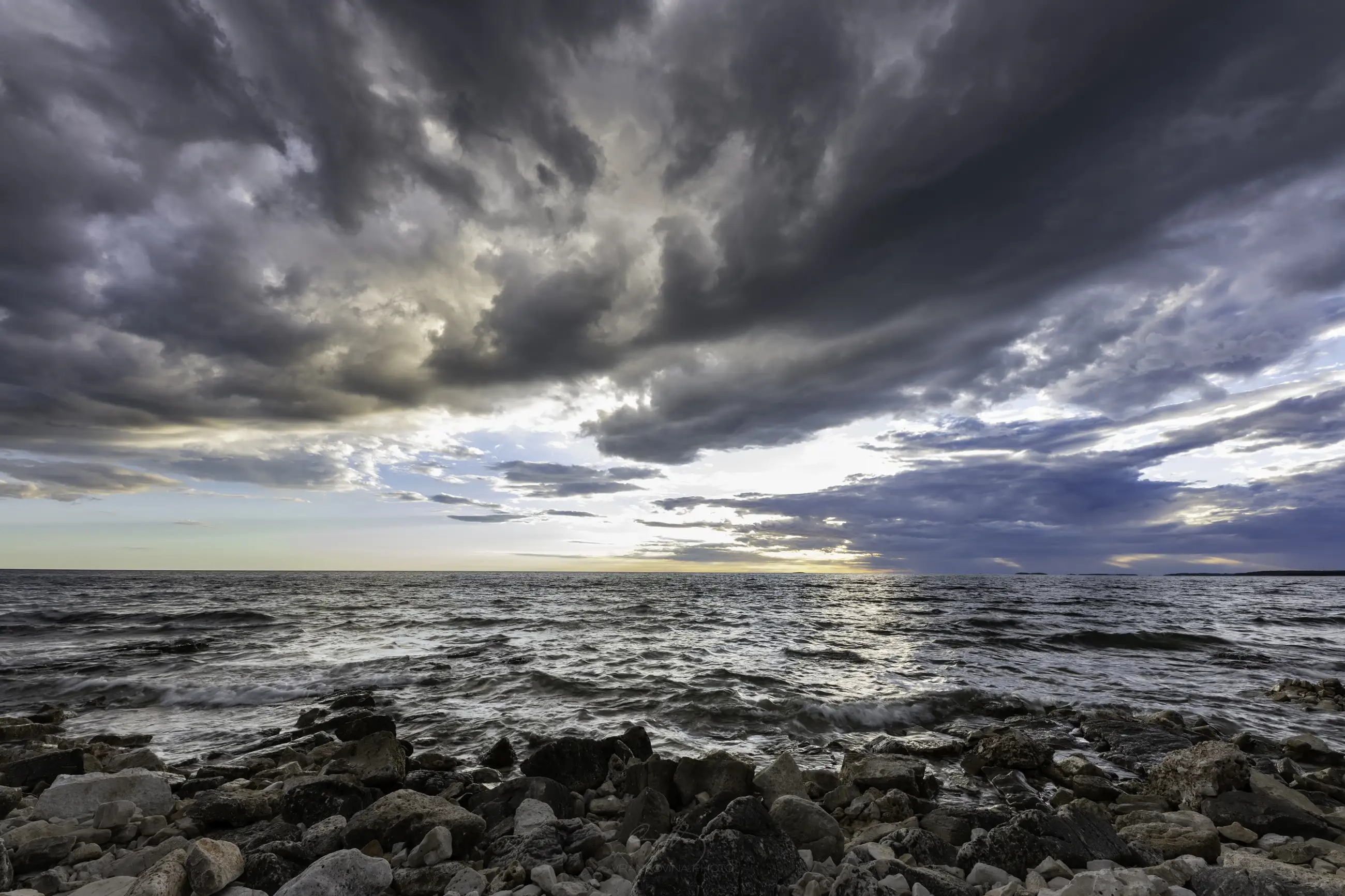 Sea horizon panorama with rocks in the foreground and cloudy sky at sunset