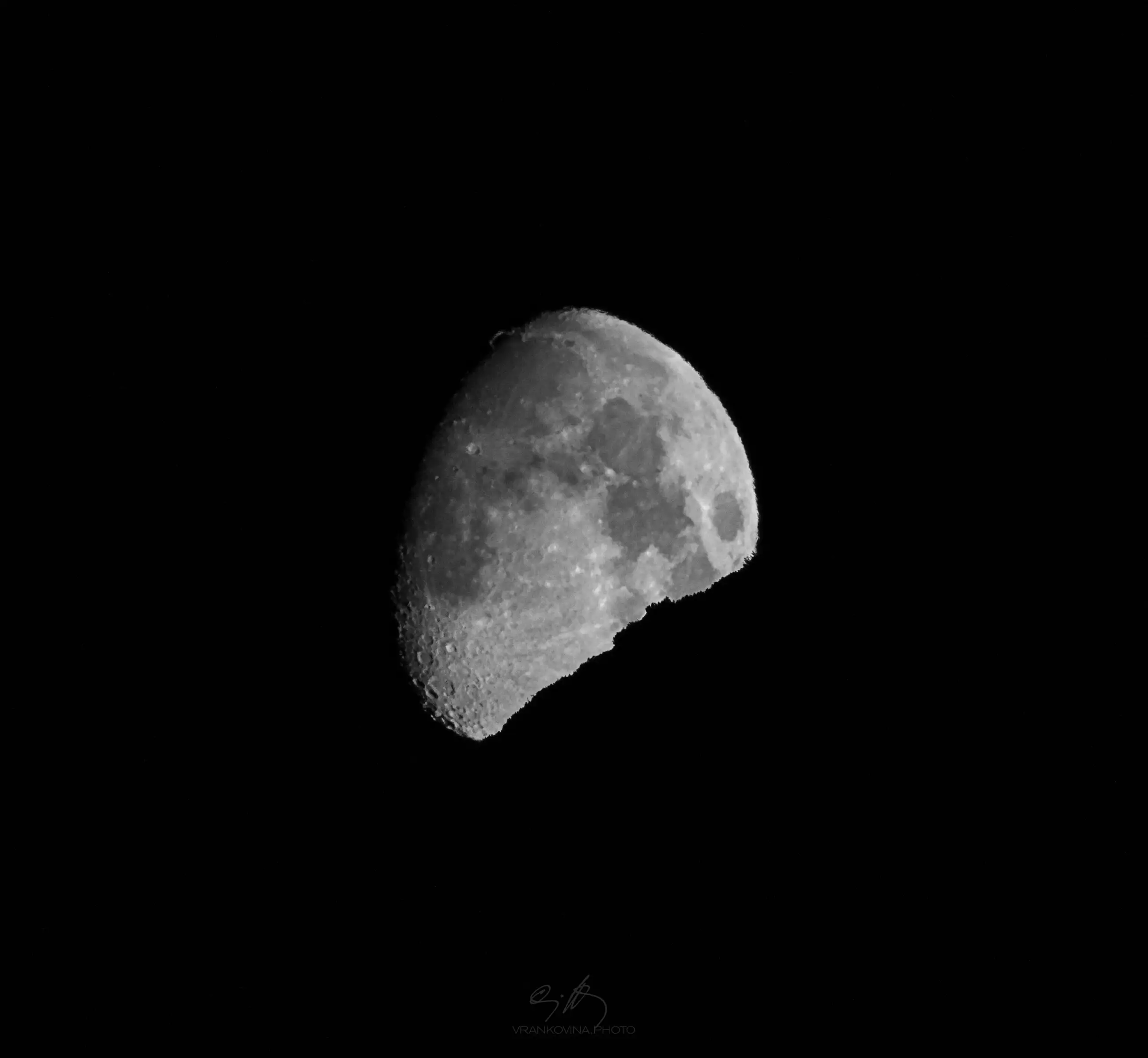A black and white photo of a waxing gibbous moon, showing detailed craters and surface textures against a dark, empty background.