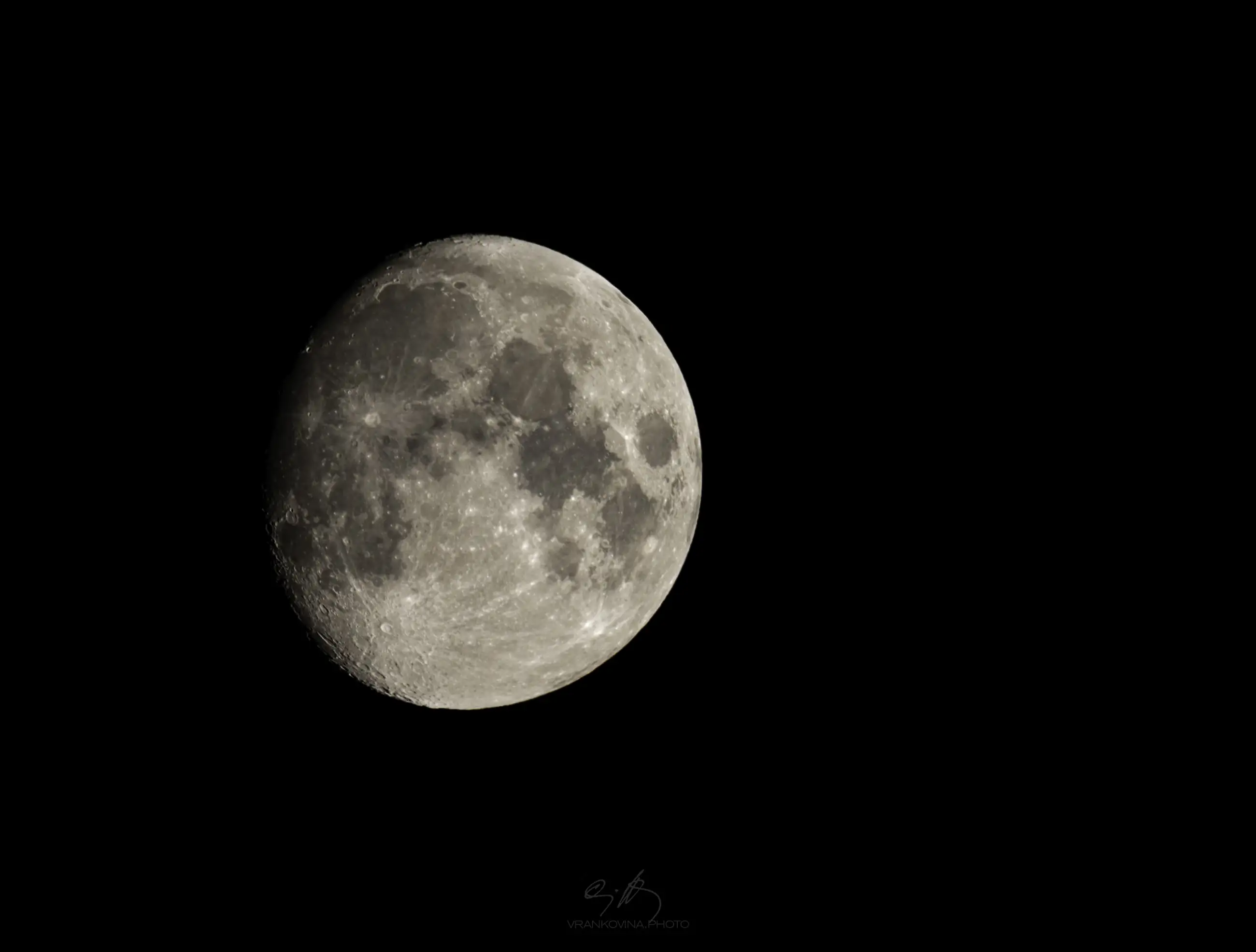 A close-up view of the moon against a black sky, showing detailed craters and surface textures. The moon is mostly full, slightly shadowed on the lower left side.